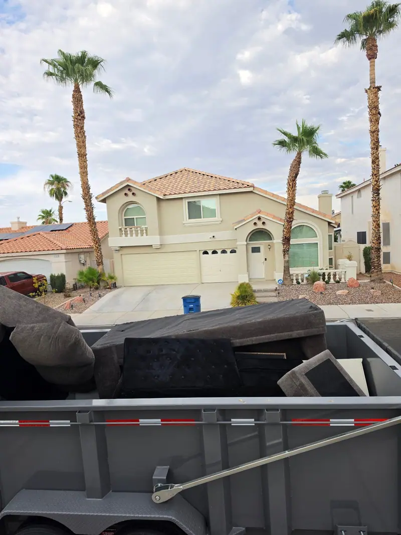Loaded trailer outside a two-story stucco home with tall palm trees