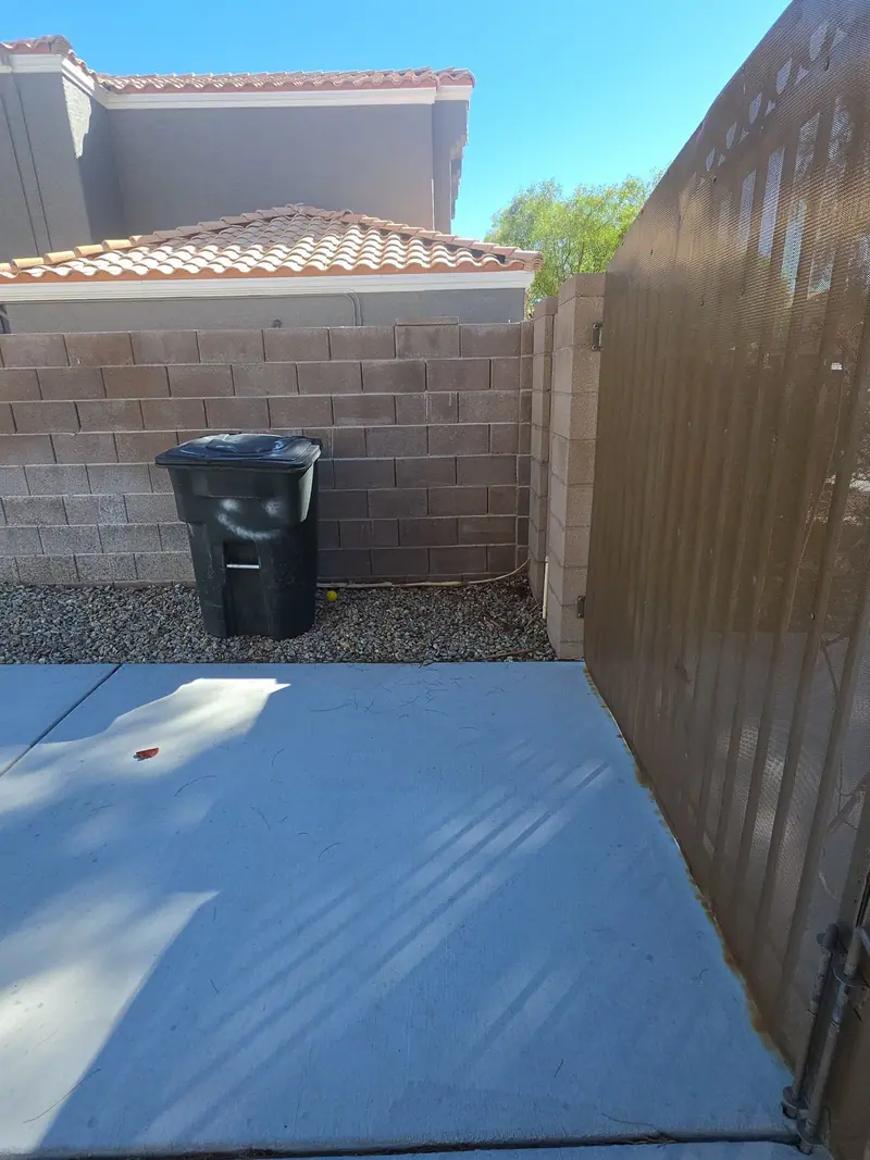 A cleared side yard with a block wall and a single trash bin after a cleanout