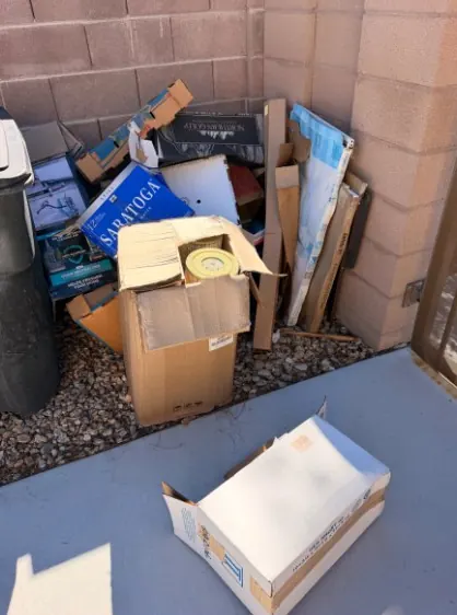 Moving boxes and cardboard stacked in a side yard corner beside the trash can