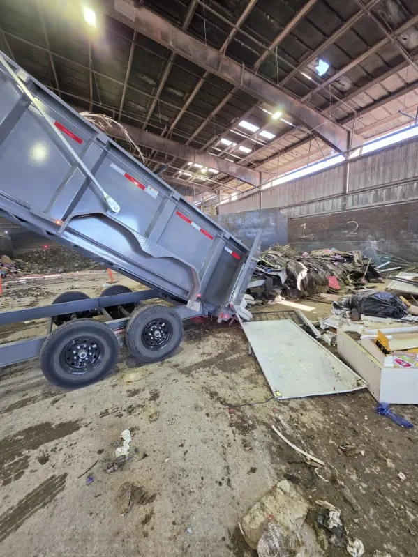 Gray dump trailer tipping a load of junk onto the floor at a transfer station