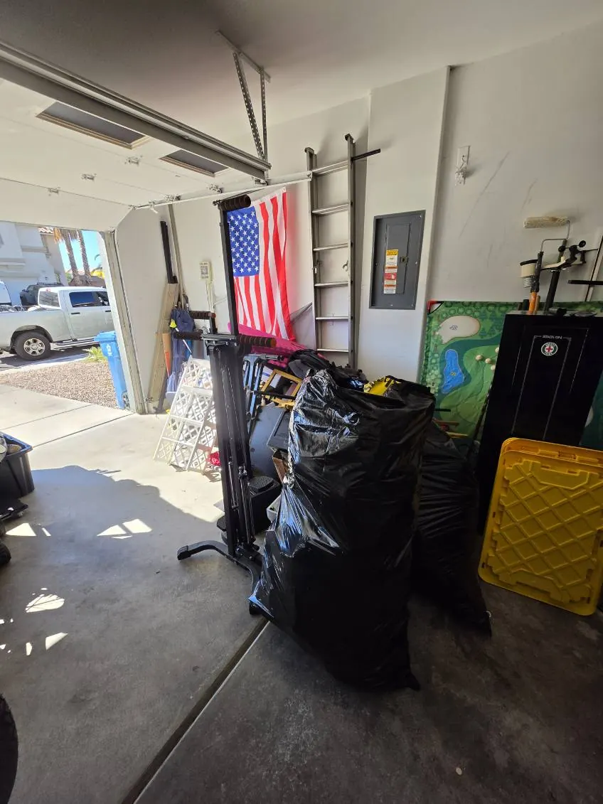 Garage before the cleanout, with black trash bags, bins, a gym rack and yellow crates by the door