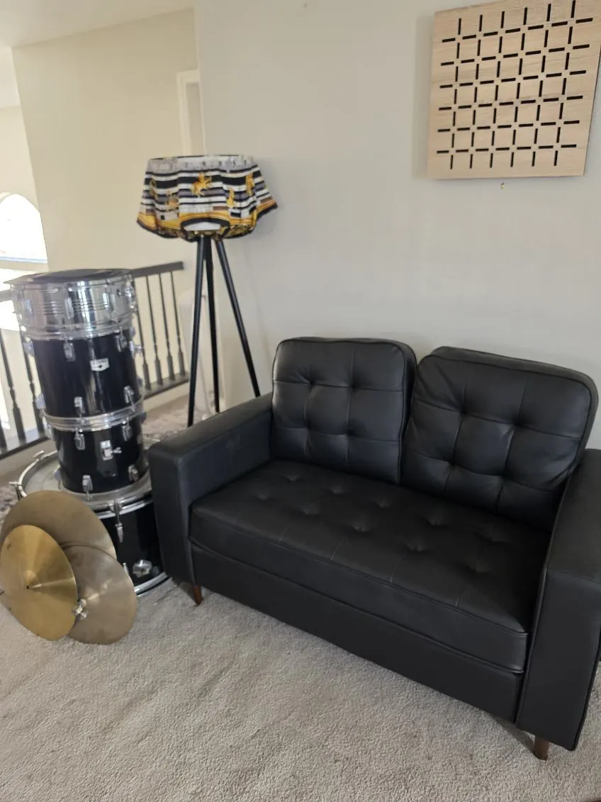 Living room with a black leather loveseat, a drum kit and cymbals