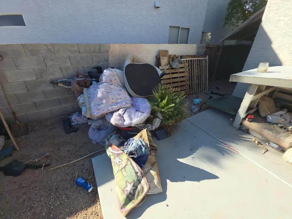 Side yard with a pile of bedding, a cushion and debris against a block wall