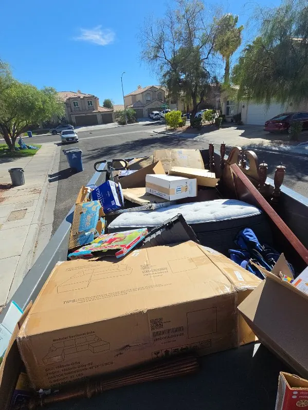 Trailer loaded with boxes, a mattress and a wooden bed frame on a residential street