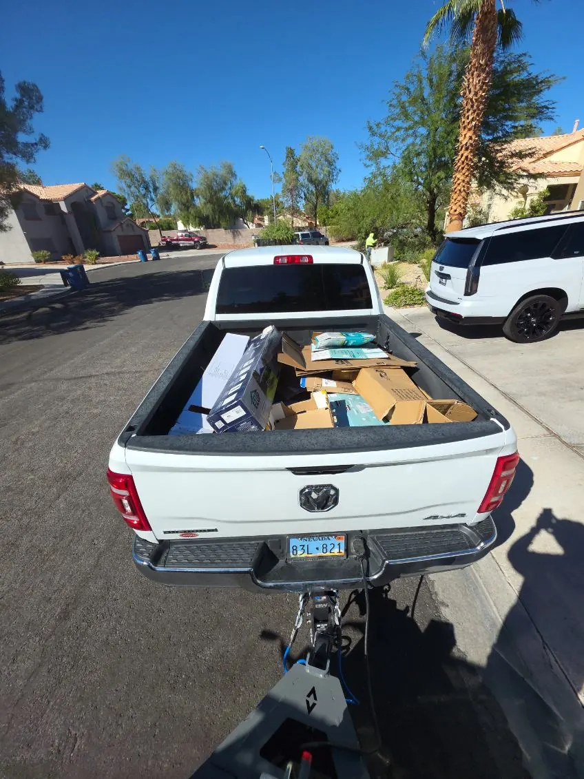 Pickup bed stacked with boxes, towing an empty trailer on a palm lined street