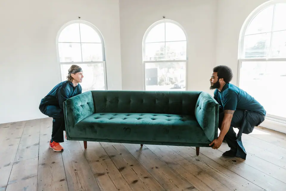 Two movers lifting a green sofa in an empty room (representative photo)