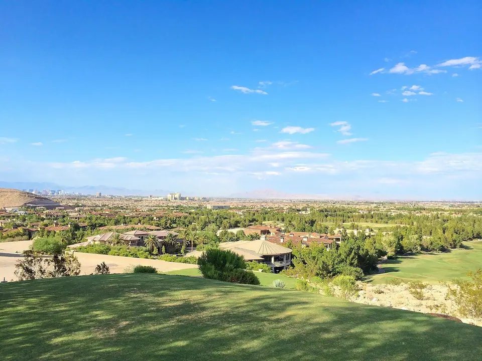 View over Enterprise from the foothills of Southern Highlands: golf-course greens and homes in the foreground, valley and distant Strip behind, daytime, Enterprise, NV